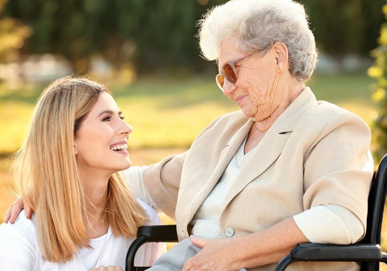 Senior woman in wheelchair and nurse from care home outdoors