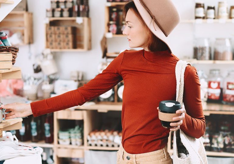 Young woman choosing products in zero waste shop. Minimalist style girl with wicker bag buying personal hygiene items in plastic free store. Customer doing shopping without plastic packaging.