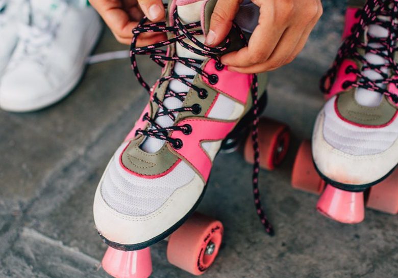 A picture of girl lying laces on her pink rollers. She has changed her white shoes to this funny rollers. Girl is almost ready to rollerblading