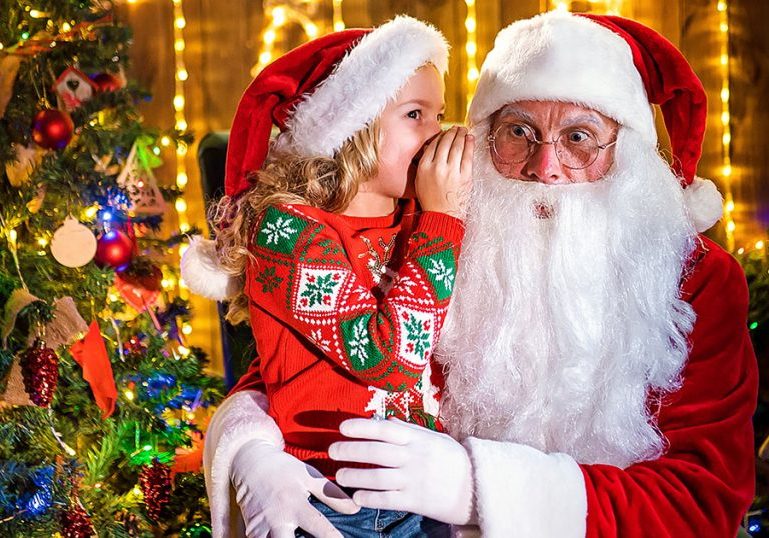 Little girl whispering in Santa's ear. Telling a secret. Revealing the gift you would like to win. Talking about how she behaved during the year.