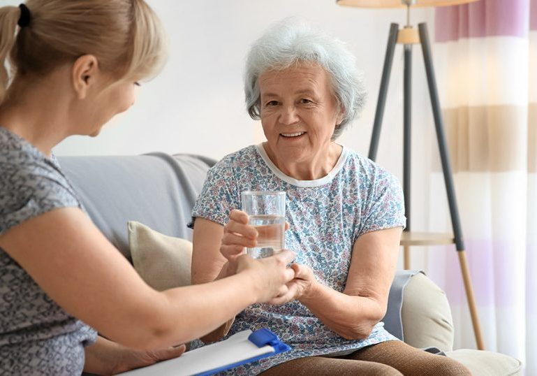 Caregiver giving glass of water to senior woman at home